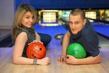 Fototapeta premium Couple lie on parquet leaning against and hold balls for bowling
