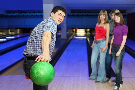 Young man prepares throw ball on path for bowling and three girl
