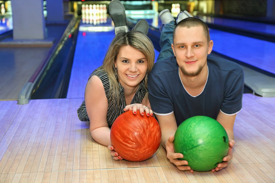 Girl and man lie on parquet in club and hold balls for bowling