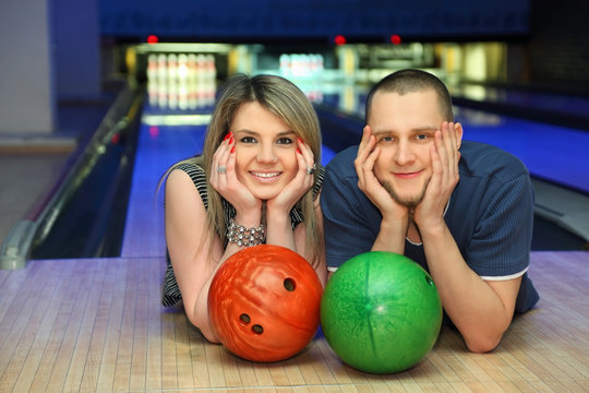 Couple lie on alongside, lean chin on hands in bowling club