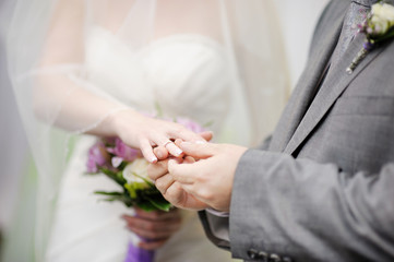 Obraz na płótnie Canvas Groom putting a wedding ring on bride's finger