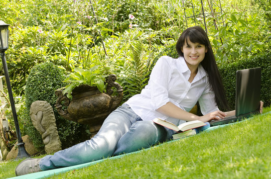 Junge attraktive Frau mit B&uuml;chern und Laptop im Garten