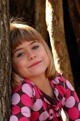 Young girl peeks from behind a tree