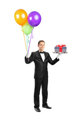 Butler carrying a tray with a gift on it and balloo