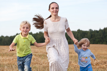 Fototapeta premium Mother and two children running outdoors smiling
