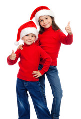 Two smiling children with thumbs up sign and Santa's hats