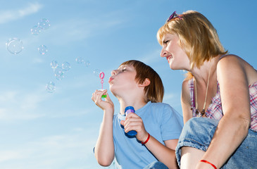 Boy and mother with soap bubbles against a sky
