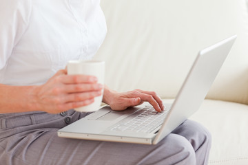 Close up of a woman holding a cup having a notebook on her lap