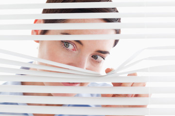 Cute businesswoman peeking through a venetian blind