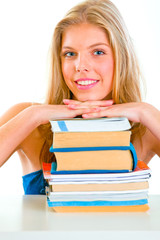 Smiling girl sitting at desk and holding hands on piles of books