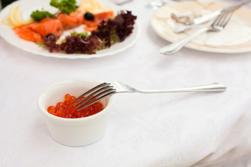 Red caviar and fork. Plates with cold snack on table