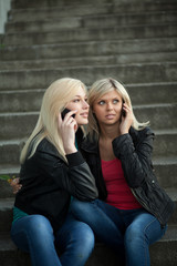 Two girls sitting on the steps with the phones and talk to fun