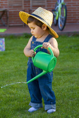little baby boy gardener watering the grass