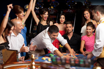 happy caucasian friends playing roulette in casino - 34834935