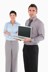 Portrait of a man showing a notebook while his colleague is posi