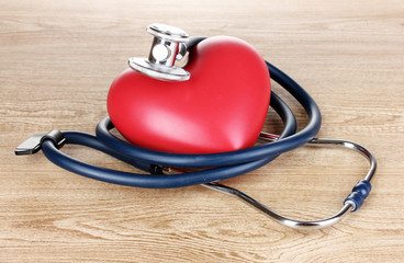Medical stethoscope and heart on wooden background