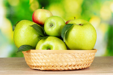 Fresh organic green apples in basket on wooden table outside
