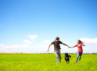 Young happy family running with dog on a green meadow