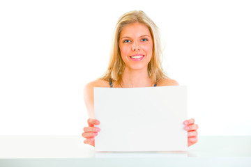 Naklejka premium Lovely girl sitting at table and holding blank paper