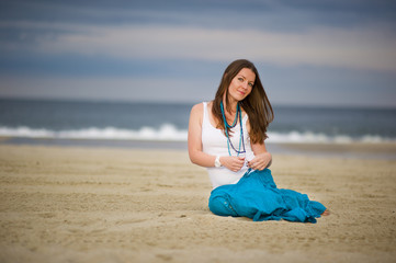 Fototapeta na wymiar Beautiful young woman sits on sand near the ocean
