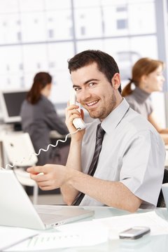 Happy businessman using laptop talking on phone