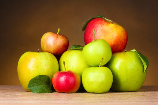 Many fresh organic apples on wooden table on yellow background