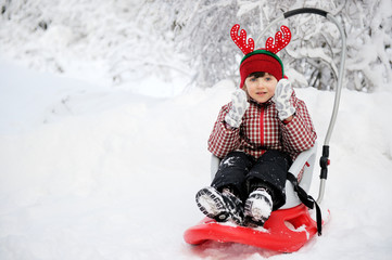 Fototapeta na wymiar Adorable child girl in horned hat sled in snow