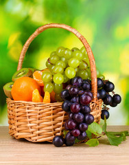 Ripe juicy fruits in basket on wooden table on green background