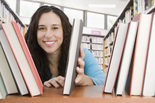 Mixed race woman looking for book in library - Powered by Adobe