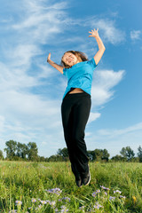 Happy girl jumps against a green grass and the blue sky