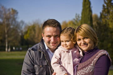 Happy family, mom and dad and little girl in the park