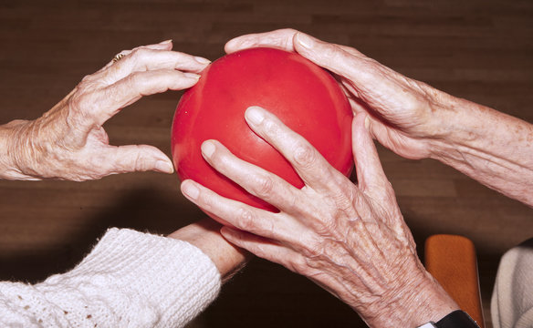 hands of seniors do gymnastics with a red ball