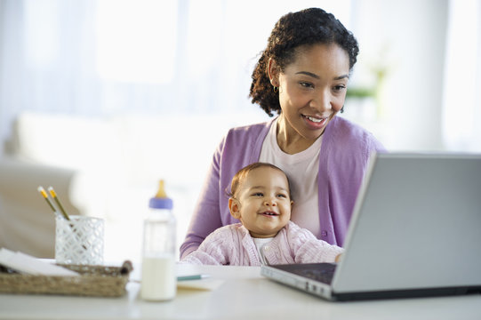 Mixed race woman holding baby and using laptop