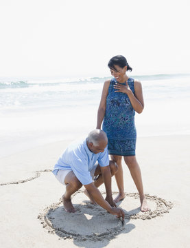 Black man drawing heart on beach for wife