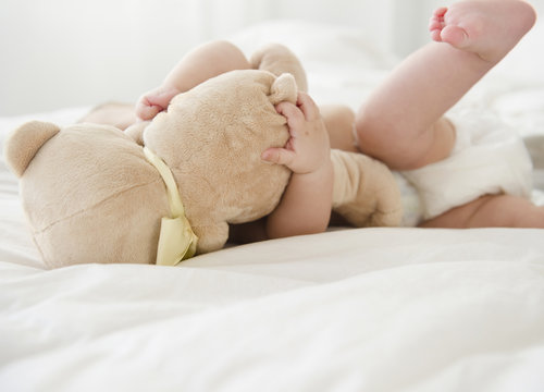Mixed race baby laying on bed with teddy bear