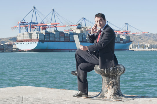 Hispanic businessman holding laptop with container ship in background