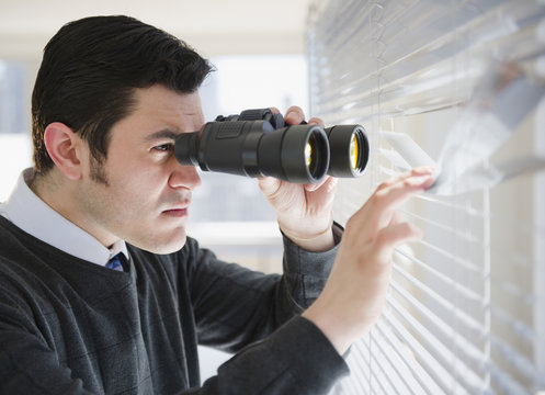 Hispanic businessman peering through window with binoculars