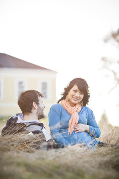 Pregnant woman sitting in field with husband