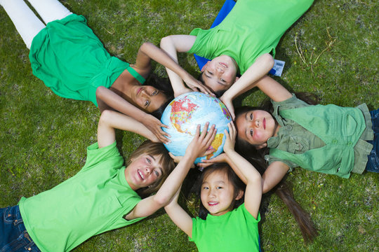 Children laying in grass around globe