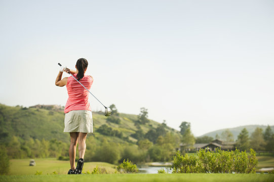 Mixed Race Woman Swinging Golf Club On Golf Course