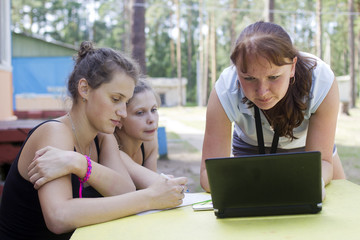 Three girls sit before the notebook and discuss something