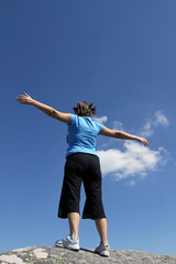 young woman with arms wide open against blue sky