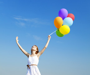 Obraz na płótnie Canvas Redhead girl with colour balloons at blue sky background.