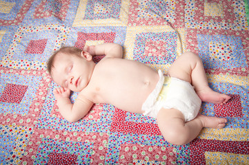 Sleeping baby boy in diaper on colorful quilt