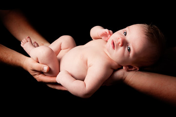 Naked baby boy held over black background