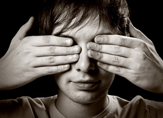 Portrait of a young man covering his eyes with hands