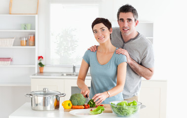 Obraz na płótnie Canvas Husband massaging his wife while she is cutting vegetables