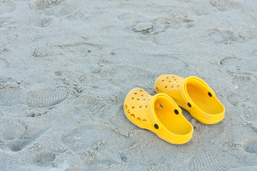 Fototapeta na wymiar Bright yellow flip-flops on sand beach