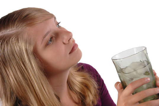 Teenage girl holding a glass of ice water looking away.