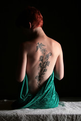 Eine Frau mit Rückentattoo bedeckt nackten Körper mit grünem Tuch
